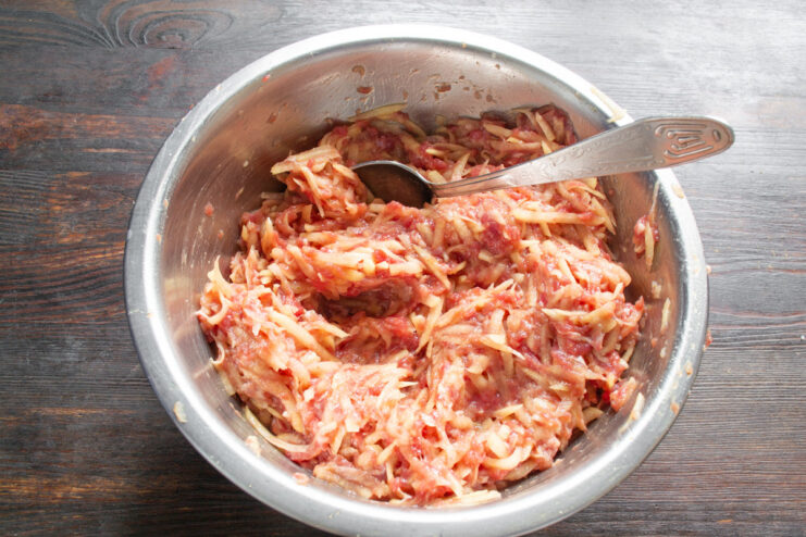 Combining Everything: Mixing the Kolduny Batter by Hand Hands in disposable gloves mixing the potato, minced meat, and seasonings in a bowl.