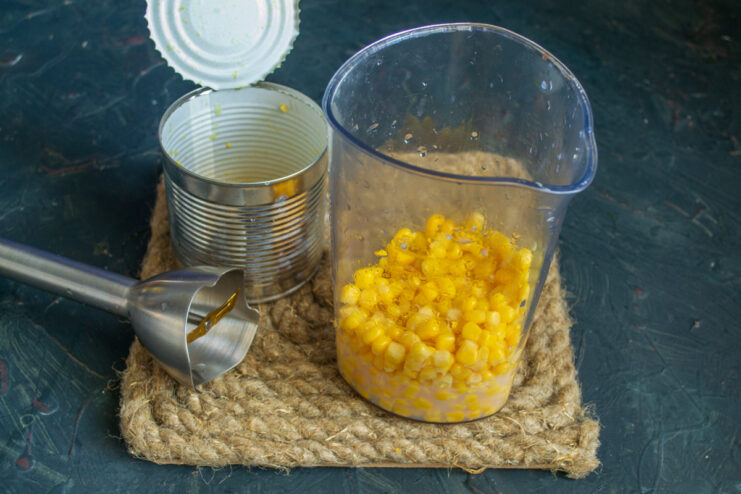 Preparing the corn base in a blender Canned corn being poured from a can into a tall blender cup.