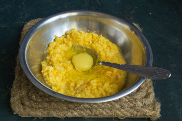 Preparing the batter for corn fritters A hand cracking an egg into a bowl with corn batter.
