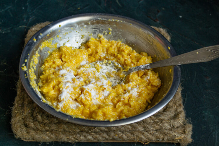 Adding leavening for fluffy fritters A spoonful of baking powder being added to the corn fritter batter.