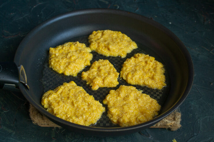 Frying the corn fritters until golden Corn fritters cooking in a frying pan on low heat.
