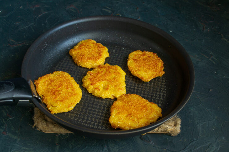 Flipping the fritters to cook the other side Flipping golden-brown corn fritters in a frying pan with a spatula.