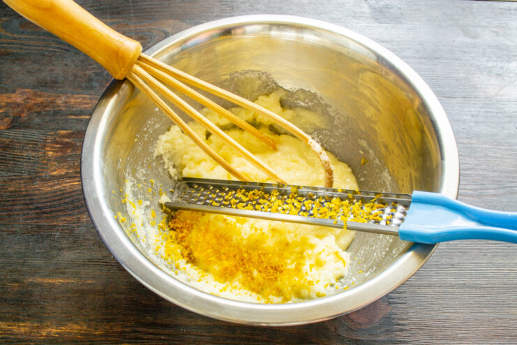 Adding fresh lemon zest for a bright, citrusy flavor. A hand grating fresh lemon zest into a bowl for the pound cake recipe.
