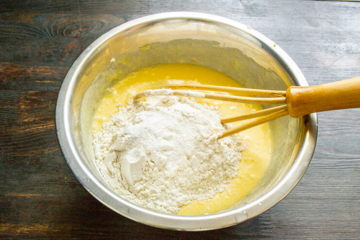 Sifting flour and baking powder for a light and airy cake texture. Sifting flour and other dry ingredients into the wet batter mixture in a bowl.