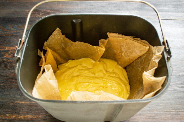 Preparing the bread machine pan for baking the pound cake. Pouring the lemon pound cake batter into a parchment-lined bread machine pan.