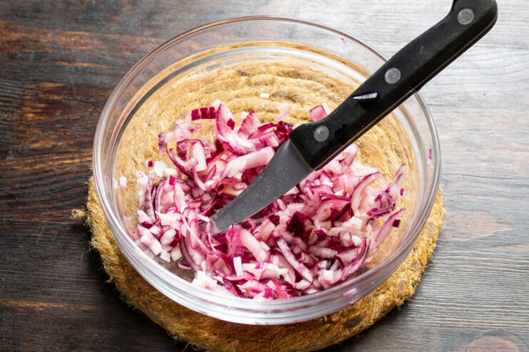 Preparing Pickled Red Onions for Garnish Chopped red onion in a bowl with apple cider vinegar being poured over it.