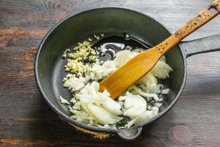 Sautéing Aromatics for the Lobio Base Chopped onion and garlic being added to a hot cast-iron skillet with oil.