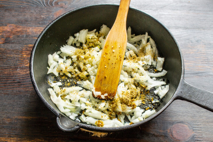 Seasoning the Onions with Khmeli-Suneli Spice Blend Spices, including khmeli-suneli, being added to sautéing onions in a skillet.