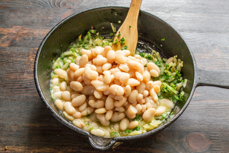 Combining Cooked Beans with the Aromatic Base Cooked white beans being added to the skillet with sautéed onions and spices.