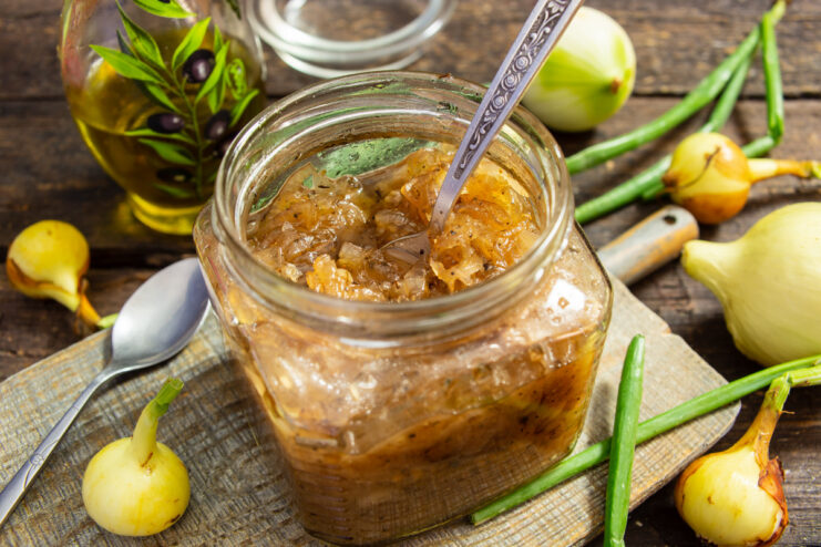 A glass jar filled with dark red onion jam with red wine, served with a spoon.