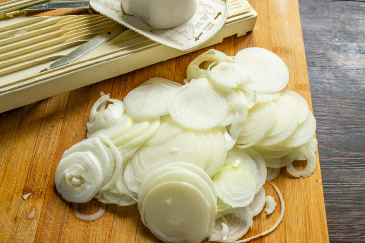 Slicing Onions for the Jam Recipe Close-up of hands peeling and thinly slicing onions into rings on a cutting board.