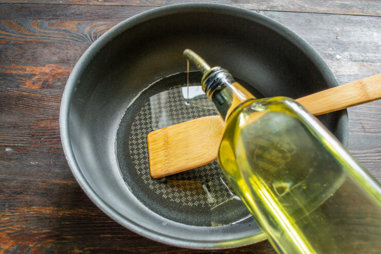 Heating Olive Oil in a Skillet Pouring olive oil from a bottle into a large, dark skillet on the stove.
