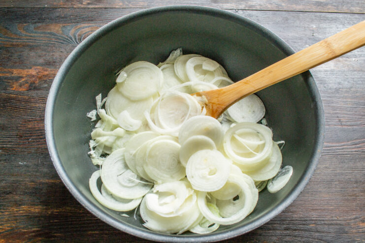 Adding Sliced Onions to the Pan A large skillet filled with thinly sliced onion rings in hot olive oil.