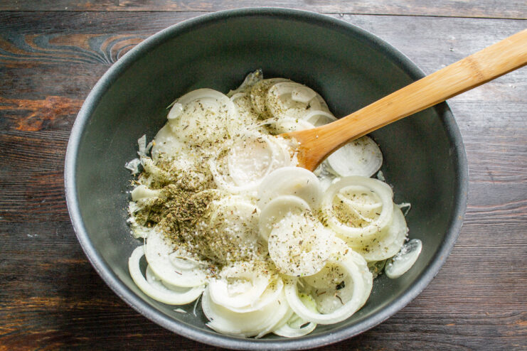 Seasoning the Onions with Herbs and Salt Adding sea salt and a blend of dried herbs to the sliced onions in the skillet.