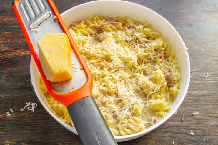 Topping the Casserole with a Generous Layer of Cheese The turkey pasta casserole in a baking dish being topped with grated cheese.