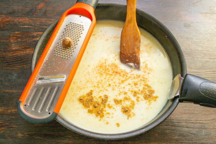 Seasoning the Sauce with Utskho-Suneli and Nutmeg Spices, including grated nutmeg, being added to the cream sauce.