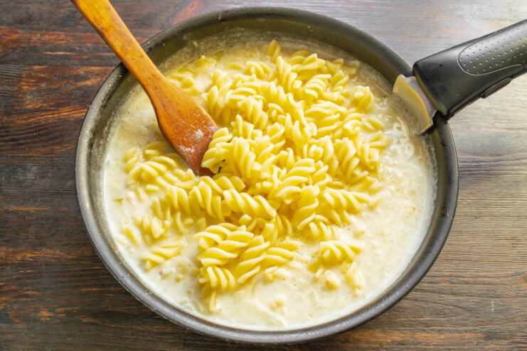 Combining Cooked Pasta with the Creamy Turkey Sauce Cooked fusilli pasta being mixed into the creamy sauce in a skillet.