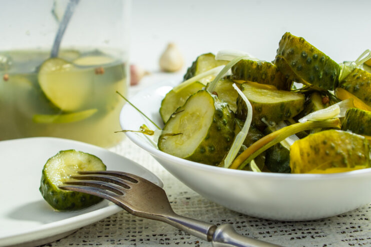 A glass jar filled with freshly made lightly salted cucumbers with slices of onion and horseradish.