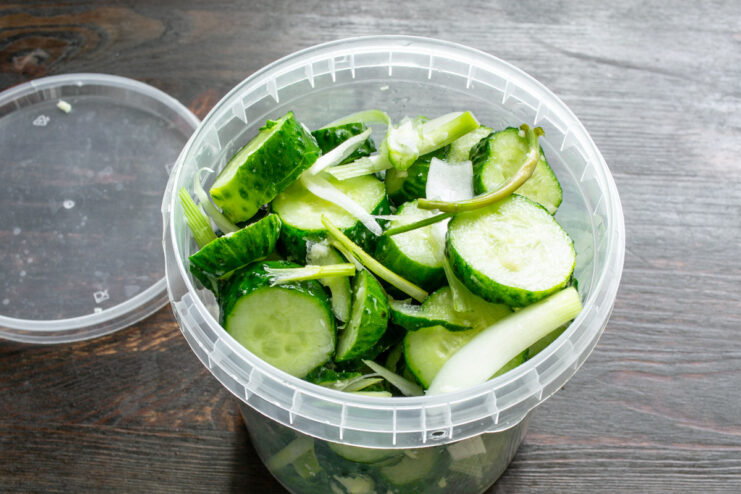 Layering Ingredients in a Jar for Fermentation Placing sliced cucumbers and other ingredients into a large glass jar.