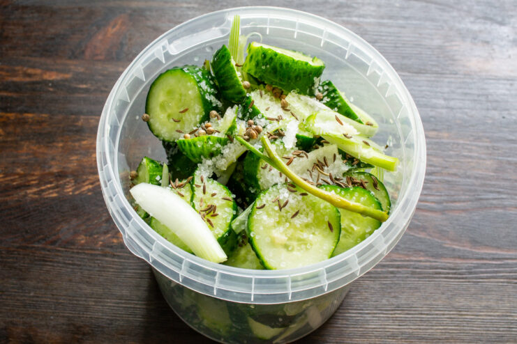 Seasoning with Coriander and Caraway Seeds Adding a spoonful of coriander and caraway seeds to the jar of cucumbers.
