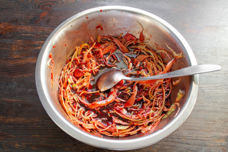 Tossing the Cabbage to Coat Evenly Mixing the shredded cabbage thoroughly with the red marinade in a bowl.