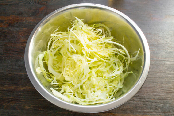 Softening the Cabbage by Hand Hands gently squeezing shredded cabbage in a large bowl to soften it.