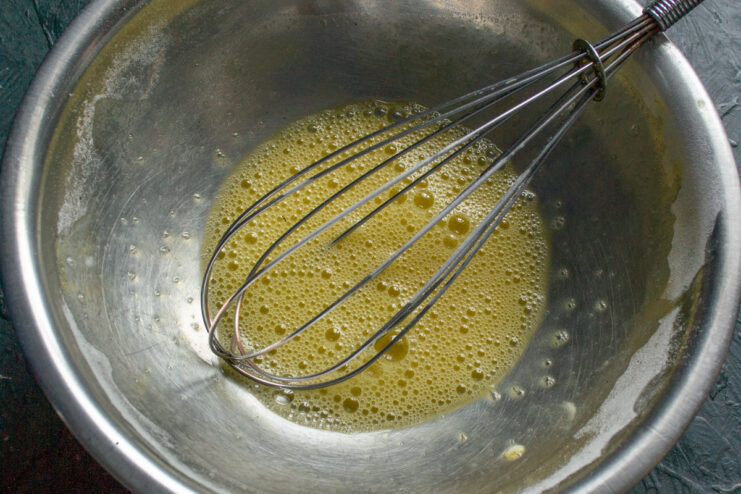 Preparing the leavening agents by whisking them with an egg. A bowl with an egg, baking powder, and baking soda being whisked together.