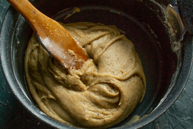 Incorporating the egg mixture into the cooled dough to finish it. Combining the cooled gingerbread dough with the whisked egg mixture.