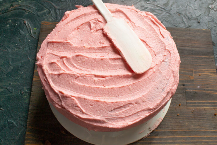 Spreading a thick layer of pink mascarpone frosting over the cooled almond cake.