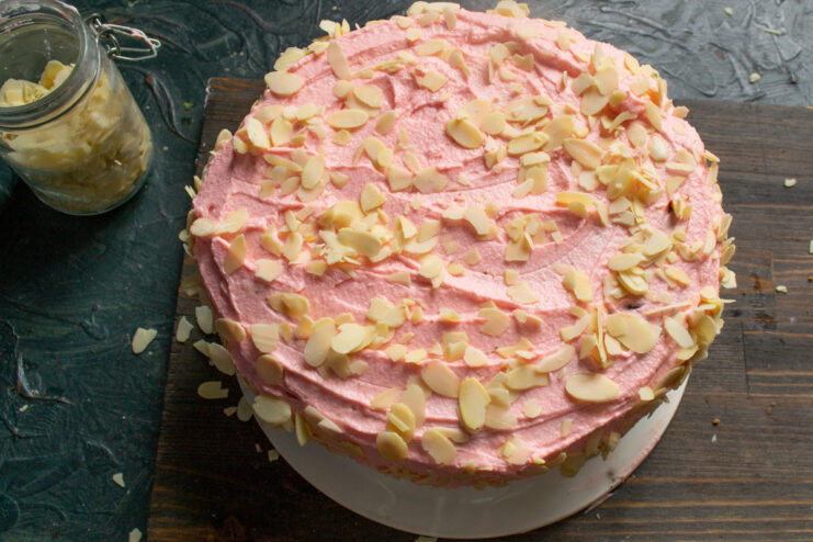 Sprinkling flaked almonds onto the sides and top of the pink-frosted almond cake.