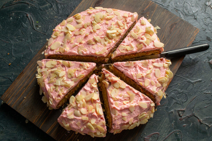 A slice of almond cake with pink frosting served on a plate, ready to be eaten.