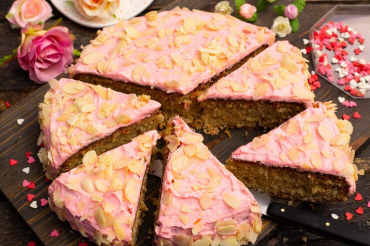 A whole almond cake decorated with pink frosting and flaked almonds on a cake stand.