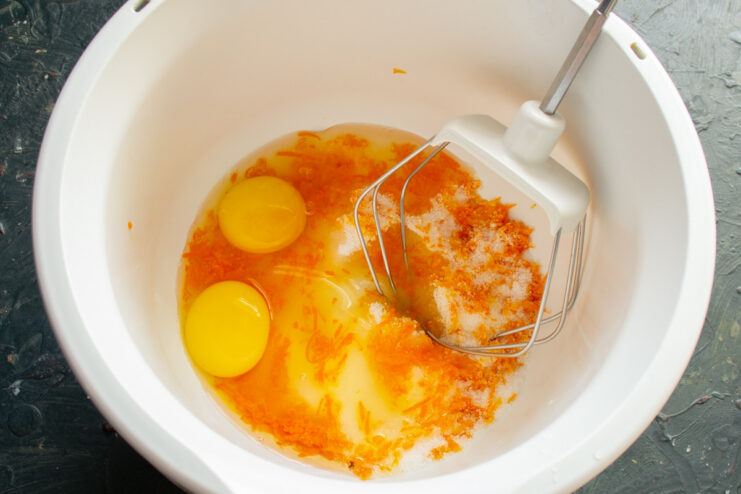 A bowl with sugar, eggs, and orange zest, ready for mixing the almond cake batter.