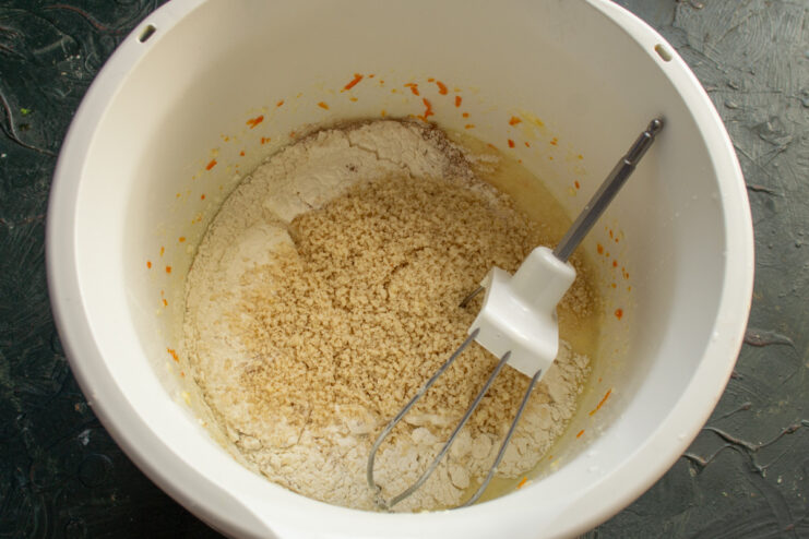 Adding ground almonds and flour to the wet ingredients in a mixing bowl.