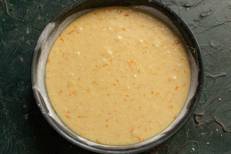 Pouring the prepared almond cake batter into a greased and floured round baking pan.