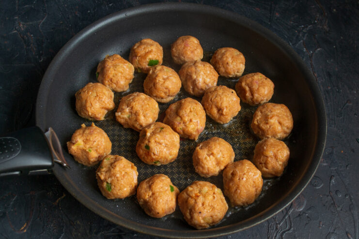 Searing the Meatballs for a Golden-Brown Crust Raw meatballs being placed in a hot frying pan with oil to be seared.