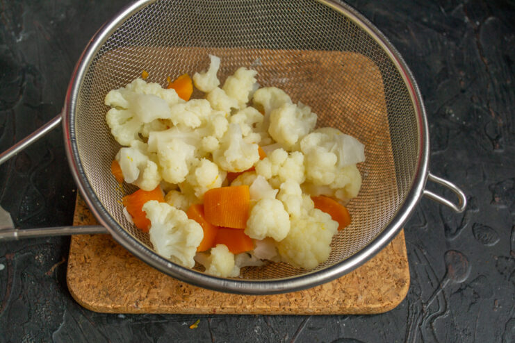 Quickly Blanching Vegetables Before Baking Blanched cauliflower and pumpkin being drained in a metal sieve over a sink.