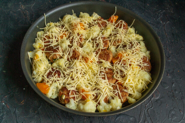Adding the Final Touch: Topping with Grated Cheese Before Baking The baking dish with meatballs and vegetables being generously sprinkled with grated cheese.