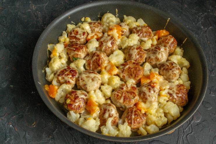 Serving the Hot and Cheesy Baked Meatballs and Vegetables A close-up of the finished dish: baked meatballs with cauliflower and pumpkin, golden and bubbly.