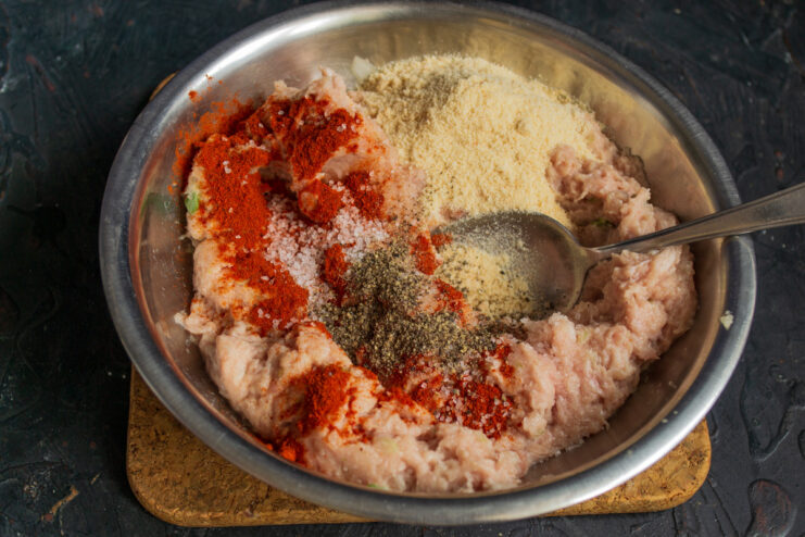 Seasoning the Meatball Mixture with Spices and Breadcrumbs Ground meat in a bowl with breadcrumbs and spices sprinkled on top before mixing.