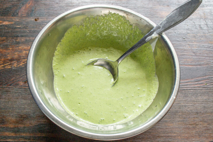 A hand blender pureeing basil, walnuts, and smetana into a creamy pesto sauce.