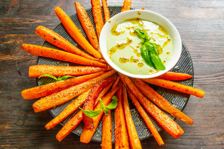 A beautiful platter of glazed fried carrots arranged in a fan shape, served with a bowl of pesto.