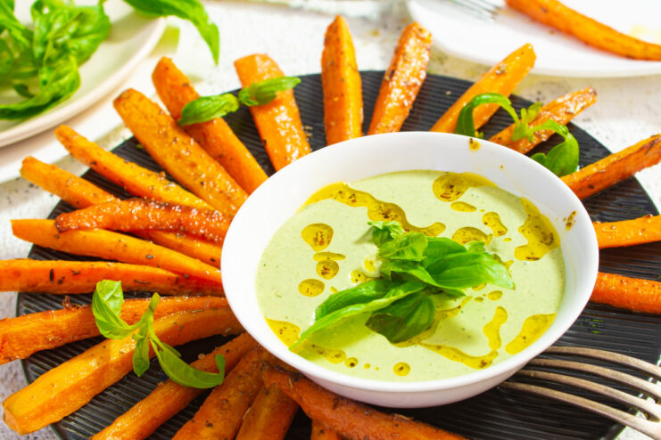 A plate of fried carrots served with a side of creamy pesto sauce in a small bowl.