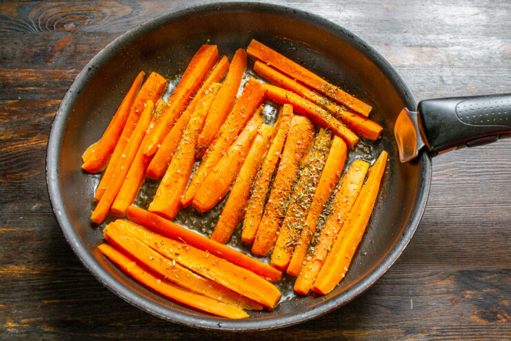 Carrot sticks being pan-fried in a skillet with herbs.