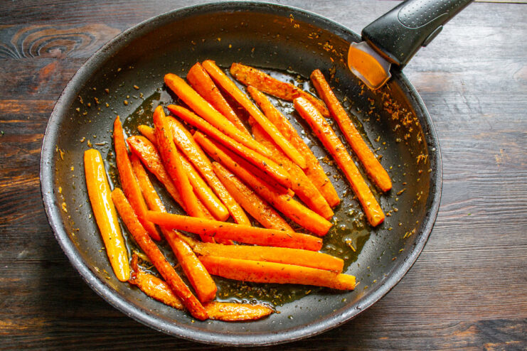 Honey and vinegar being added to the carrots in the skillet to create a glaze.