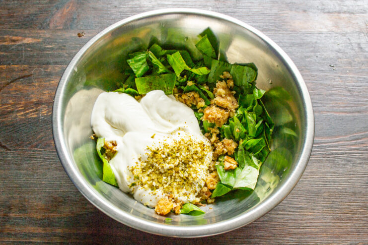 A spoonful of creamy smetana being added to the pesto ingredients.
