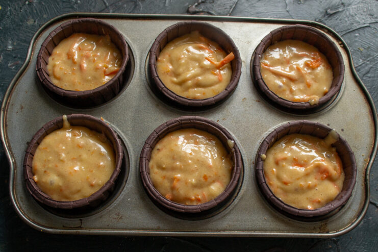 Portioning the batter into muffin liners. Muffin batter being scooped into paper liners in a muffin tin.