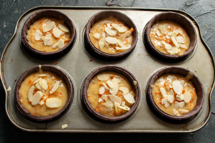 Topping the muffins with almonds before baking. Unbaked carrot muffins in liners, topped with sliced almonds.