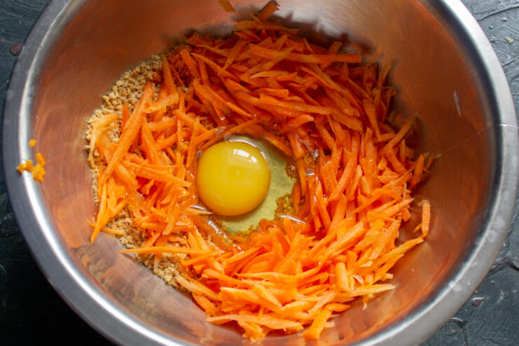 Adding an egg to the muffin batter. A large egg being cracked into a bowl of ingredients.