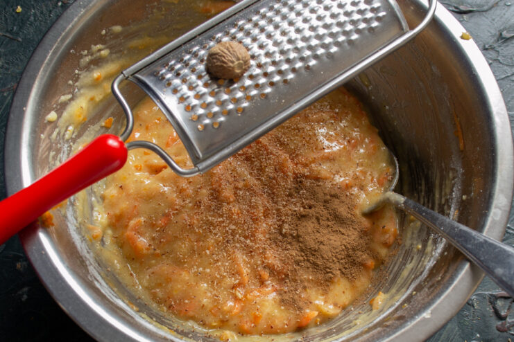 Spicing the batter with cinnamon and fresh nutmeg. Spices, cinnamon and freshly grated nutmeg, being added to the muffin batter.